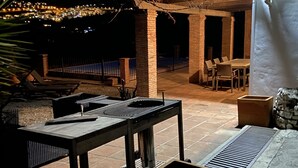 An outdoor patio area with a grill, seating, and a view of a cityscape at night. - Beautiful holiday home in the heart of Andalucia, A/C, Private Pool, WiFi. (Cómpeta)
