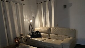 A living room with a beige sofa, a small round table with a woven basket, a floor lamp, and a key on the wall. - Beautiful holiday home in the heart of Andalucia, A/C, Private Pool, WiFi. (Cómpeta)
