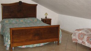 A bedroom with a wooden bed, a nightstand with a lamp, and a small table with a floral tablecloth.