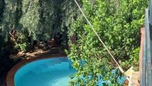 A swimming pool surrounded by lush greenery, a wooden bench, and a brick wall. - Apartment in villa Mora near the sea - Wi-fi (Avola)
