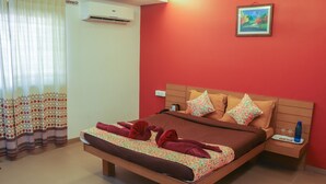A bed with a floral bedspread, a brown headboard, and multiple pillows. There is a nightstand with a water bottle and glasses. - Surya Kiran Miramar (Panaji)
