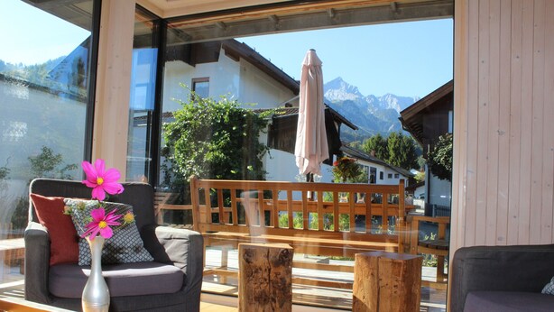 A modern outdoor seating area with a wooden bench, a cushioned chair, and a wooden table. - Exclusive Mondholz vacation apartment in a very quiet and central location in Garmisch (Garmisch-Partenkirchen)