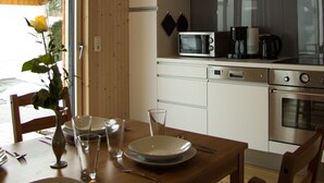 A wooden dining table set with plates, glasses, and cutlery, a vase with flowers, and a hanging light fixture. - Exclusive Mondholz vacation apartment in a very quiet and central location in Garmisch (Garmisch-Partenkirchen)