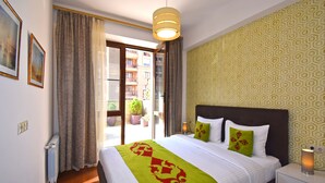 Una habitación de hotel con una cama, una mesita de noche, una lámpara, un ventanal con cortinas y un papel tapiz estampado.