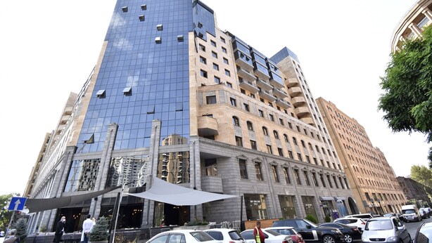 Un edificio de varios pisos con una mezcla de estilos arquitectónicos modernos y clásicos, destacando una fachada de vidrio y una serie de balcones.