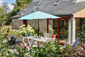 Ein Steinhäuschen mit Terrasse, Sitzgelegenheiten im Freien und einem großen Sonnenschirm.