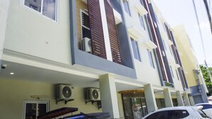 A multi-story building with air conditioning units mounted on the exterior wall, a glass entrance, and a parked car in front. - ELTI Suites (Angeles City)