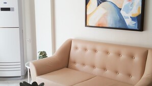 A living room with a beige sofa, a glass coffee table, and a modern painting on the wall. - ELTI Suites (Angeles City)