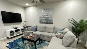 A modern living room with a grey sofa, a coffee table, a TV, and a painting on the wall. - Cozy home near Medical Center & NRG Stadium - B (Houston)