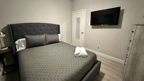 A bedroom with a bed, a TV mounted on the wall, a door, and a wooden cabinet. - Cozy home near Medical Center & NRG Stadium - B (Houston)