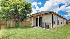 A single-story house with a covered porch, a fenced backyard, and a large tree. - Cozy home near Medical Center & NRG Stadium - B (Houston)