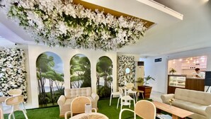 A room with a green artificial grass floor, white furniture, and a ceiling adorned with white flowers. There are three large windows with a view of trees. - HOTEL EUROASIA (Angeles City)
