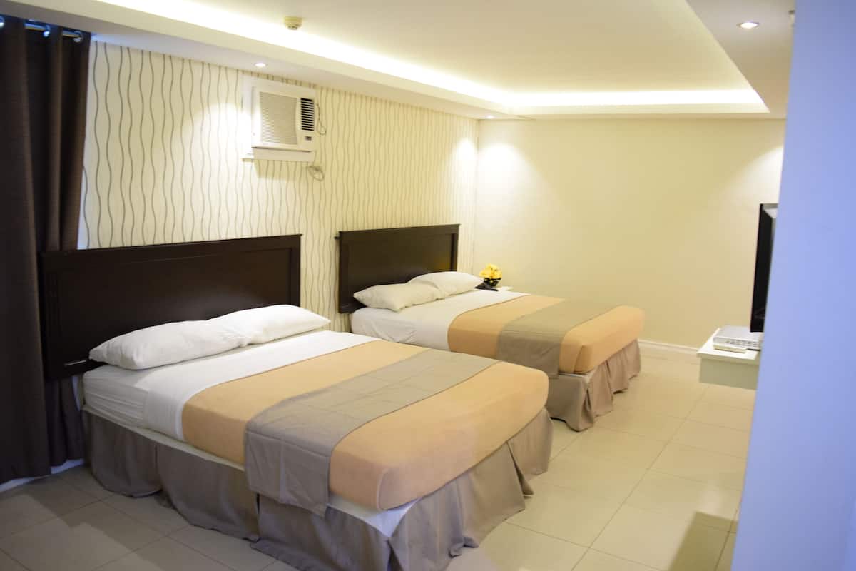 A hotel room with two beds, a bench, a small table, and a wall-mounted air conditioner.