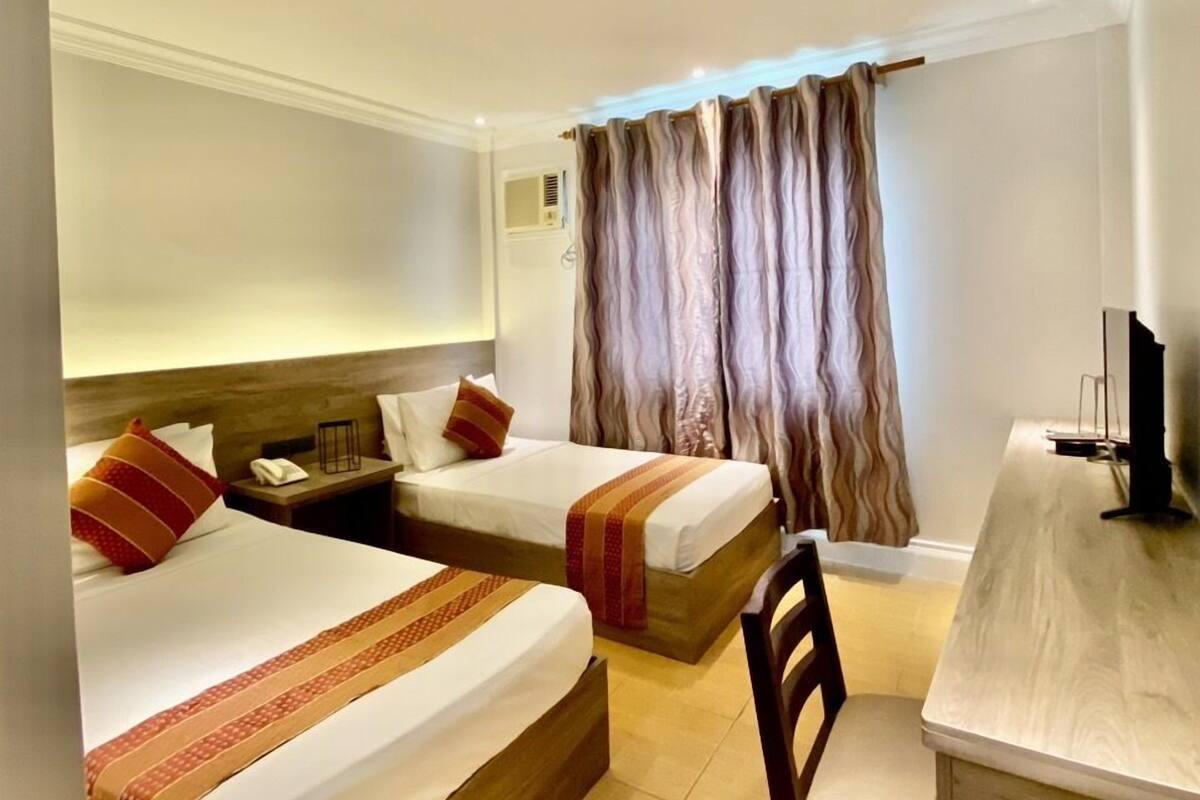 A hotel room with two beds, a desk, a chair, and a television.