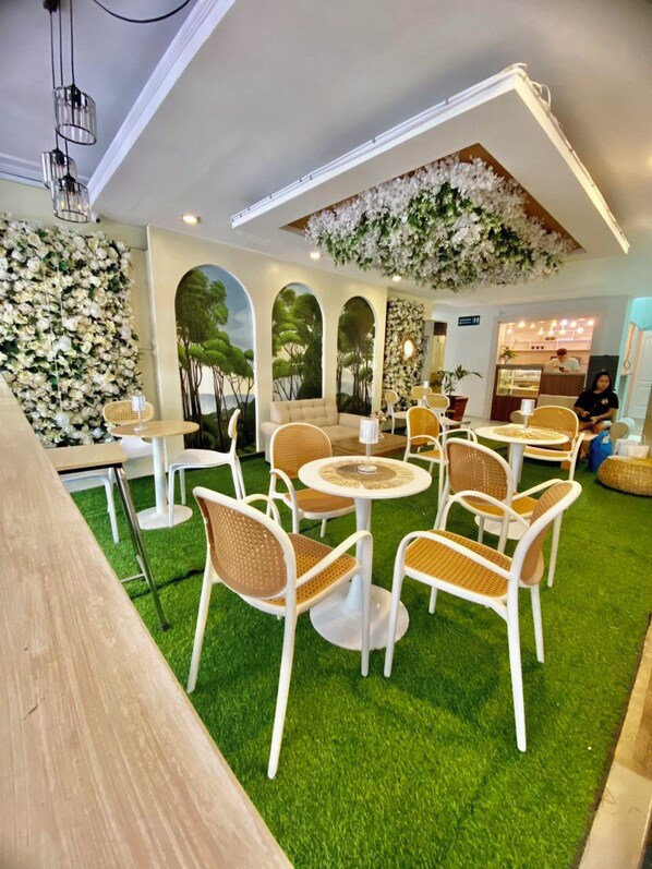 Un interior de restaurante con mesas redondas, sillas de mimbre y un piso de césped artificial verde.