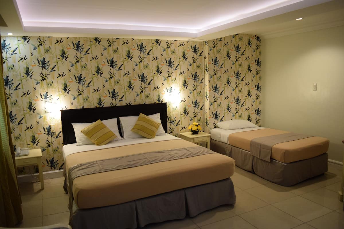 A hotel room with a large bed, a smaller bed, a nightstand with a lamp, and a wall with a leafy pattern.