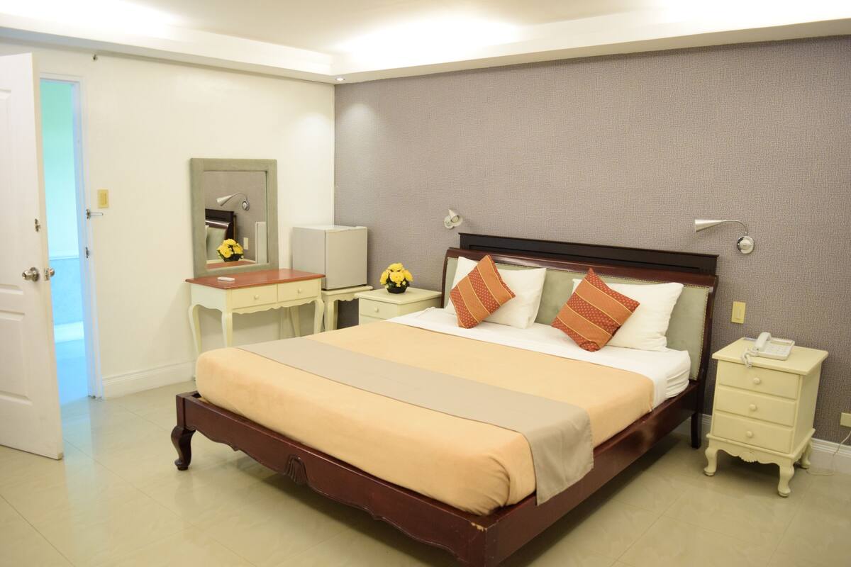 A neatly arranged hotel room with a large bed, bedside tables, a desk, and a mirror.