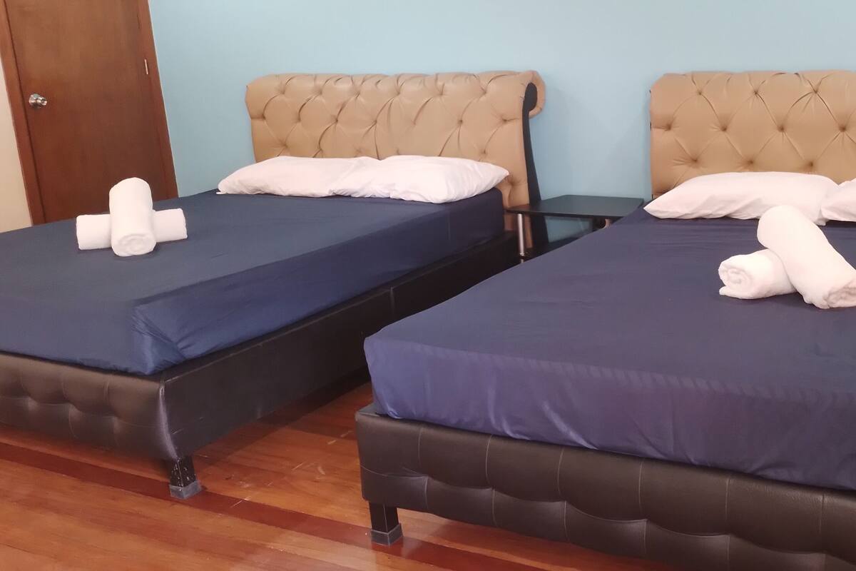 Duas camas com roupa de cama azul escura e cabeceiras bege, cada uma com toalhas brancas dobradas.