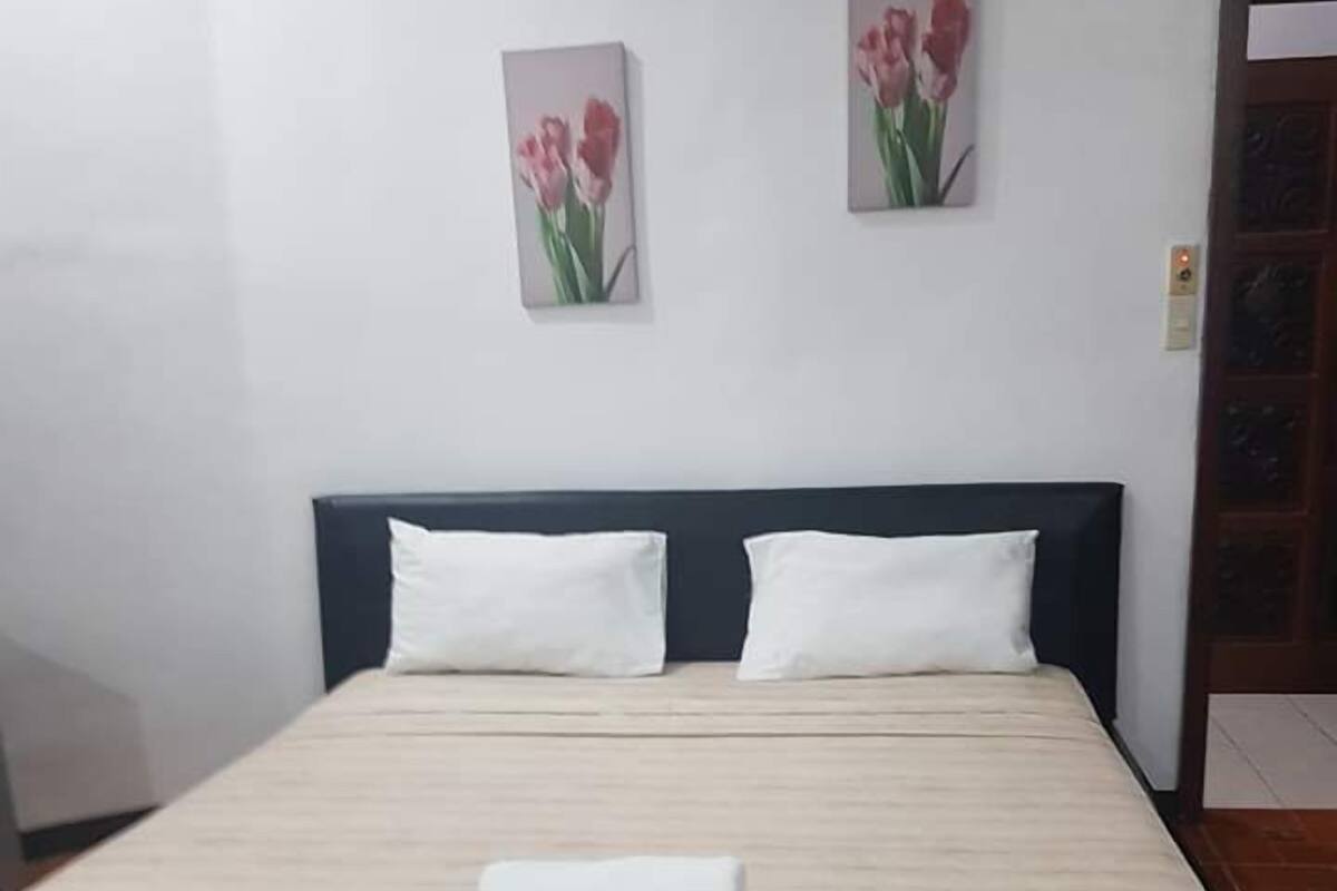Uma cama bem arrumada com lençóis e almofadas brancos, uma toalha enrolada e duas fotos emolduradas de flores na parede.