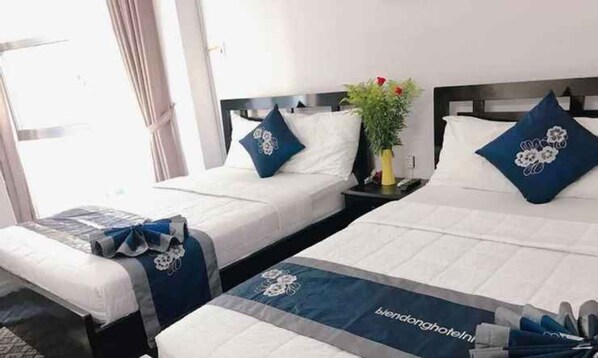 A hotel room with two beds, each with a blue floral pillow and a matching bed runner. A small table with a vase of flowers is between the beds. - Ximao Hotel Nha Trang by Zuzu (Nha Trang)