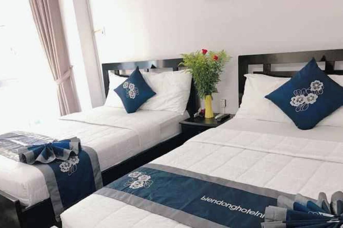 A hotel room with two beds, each with a pillow and a bedside table.