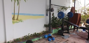 A gym with a wall mural of a beach, a squat rack, and blue dumbbells on the floor. - Ximao Hotel Nha Trang by Zuzu (Nha Trang)
