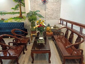 A living room with a blue sofa, wooden chairs, a coffee table, and a decorative plant. - Ximao Hotel Nha Trang by Zuzu (Nha Trang)