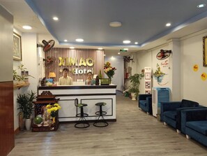 A hotel reception area with a reception desk, two bar stools, a blue sofa, and a wall with a sign that reads "XIMAO Hotel". - Ximao Hotel Nha Trang by Zuzu (Nha Trang)