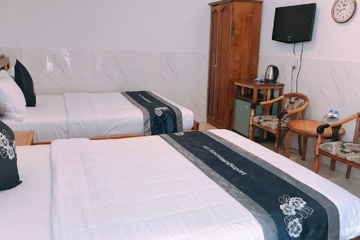 Ein Hotelzimmer mit zwei Betten, einem Holzschrank, einem Fernseher und einem kleinen Tisch mit Stühlen.