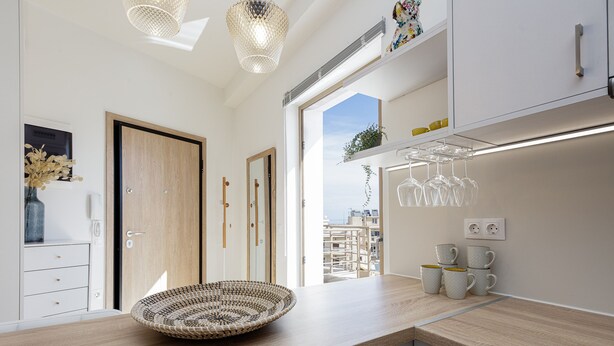 A modern kitchen with a wooden countertop, a woven basket, and a view of the city through a large window.