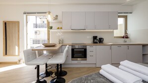 A modern kitchen with white cabinets, a built-in oven, and a wooden countertop. There is a bar stool and a window providing natural light.