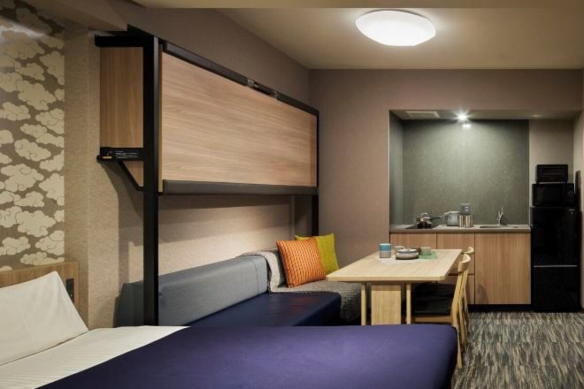 A compact hotel room with a bed, a small kitchenette, and a seating area with a table and chairs.