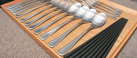 Una bandeja de madera con diversos utensilios, como tenedores, cucharas y palillos.