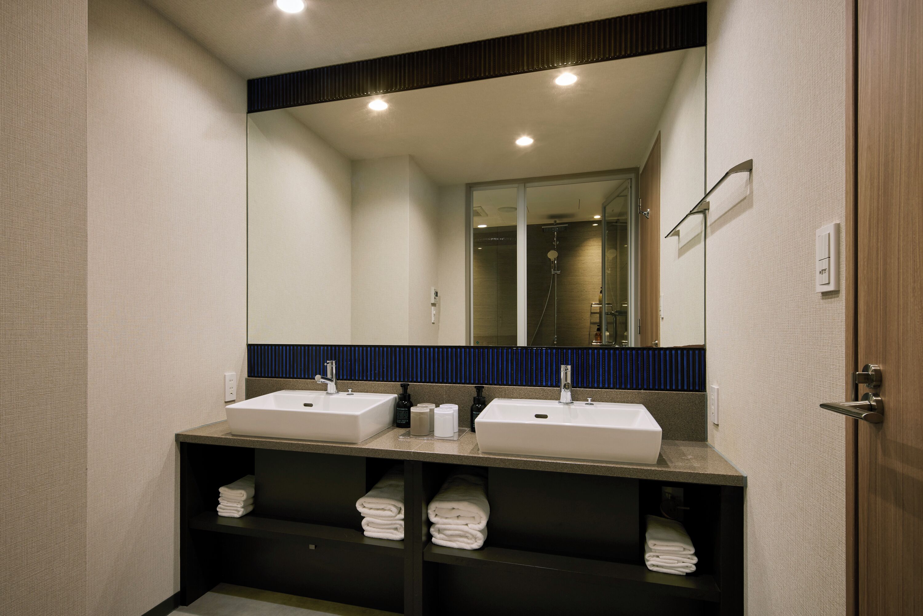 Ein modernes Badezimmer mit zwei Waschbecken, einem großen Spiegel und Regalen mit gefalteten Handtüchern.