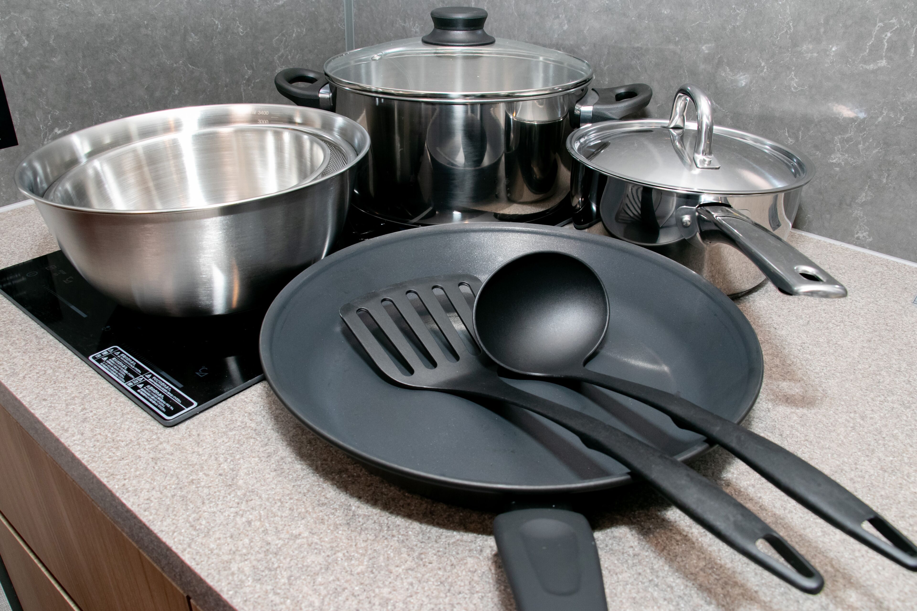 Una encimera de cocina con utensilios de acero inoxidable, incluyendo ollas, sartenes y una sartén con espátula y cuchara.