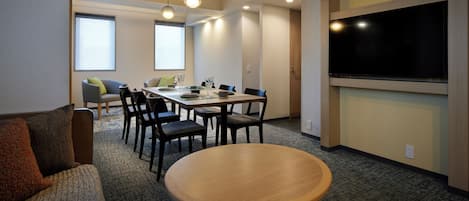 Une salle de conférence équipée d’une table ronde, d’une table rectangulaire et de chaises. Un téléviseur est fixé au mur et un appareil de climatisation est installé au-dessus de la table.