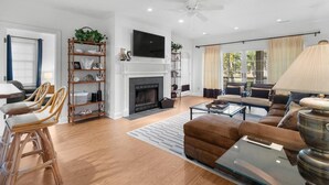 Un salon moderne avec une cheminée, un téléviseur fixé au-dessus, et un ventilateur de plafond. On y trouve deux canapés, une table basse et un coin repas avec des chaises.
