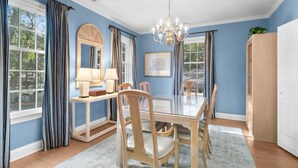 Une salle à manger avec une table en verre, des chaises en bois, un lustre et une grande fenêtre avec des rideaux.