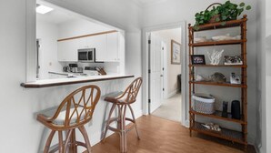 Une cuisine moderne avec des meubles blancs, un four à micro-ondes et un coin bar équipé de deux chaises en bois.