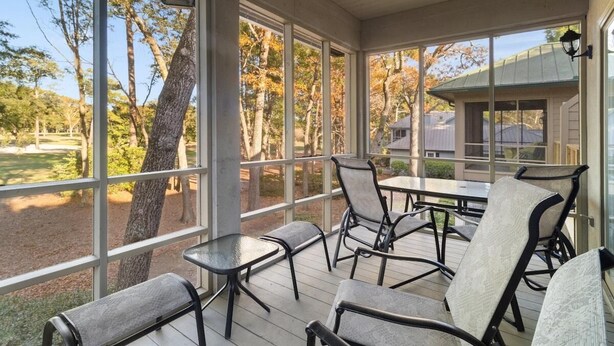Une terrasse couverte avec une table et des chaises, de grandes fenêtres et une vue sur des arbres et un bâtiment.