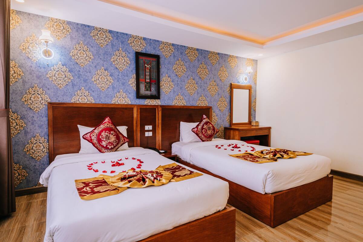 Ein Hotelzimmer mit zwei Betten, einem Holzkopfstück, einer Wand mit einem Muster und einem gerahmten Bild über den Betten.