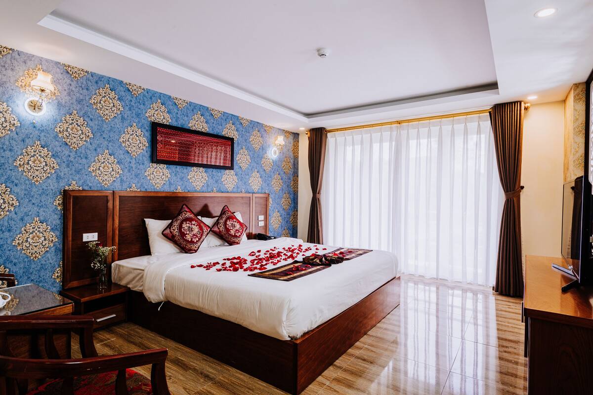 Ein Hotelzimmer mit einem großen Bett, einem Holzkopfteil und einem an der Wand montierten Fernseher.