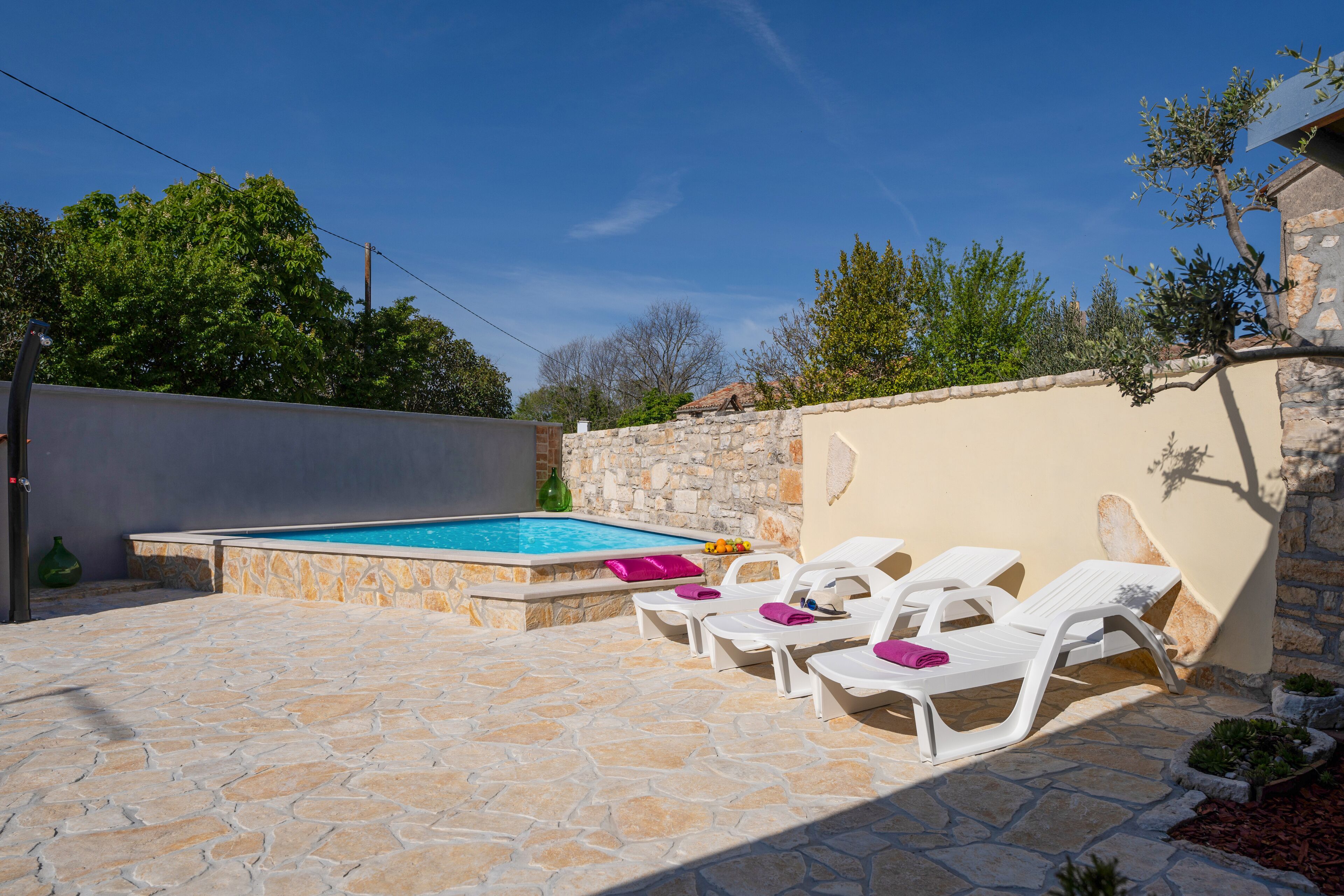 Un espace piscine doté d’un sol en pierre, de chaises longues blanches et d’un mur en pierre.
