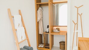 A wooden walk-in closet with hanging robes, a shelf with shoes, and a small table with a basket. - Cape by Sichon Tesoro (Sichon)