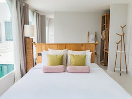 Habitación de hotel con una cama grande, cabecera de madera, vista a una piscina y una escalera de madera.