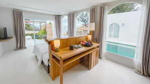 A hotel room with a wooden desk, a bed, a TV, and a view of a swimming pool. - Cape by Sichon Tesoro (Sichon)