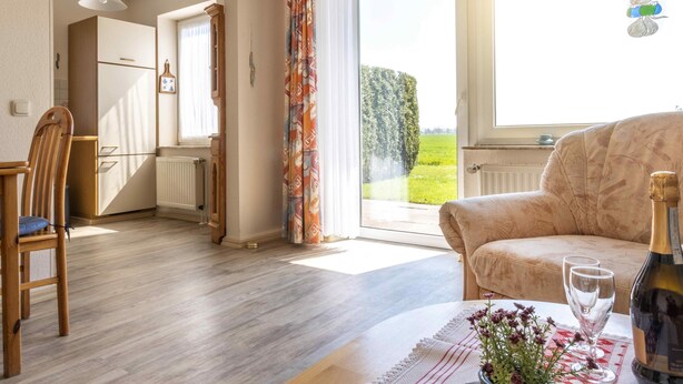 Un salon avec un canapé, une table à manger avec des chaises, une fenêtre donnant sur un paysage verdoyant et une bouteille de champagne posée sur la table.