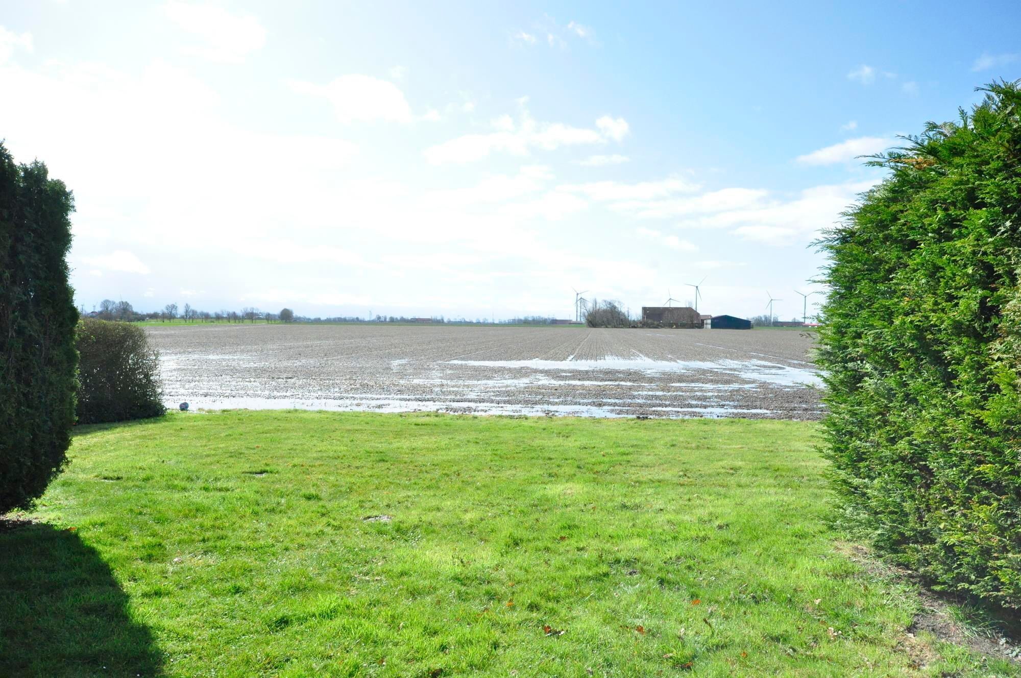 A rural landscape with a plowed field, a barn, and wind turbines in the distance.