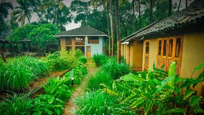 A traditional house with a tiled roof and wooden doors, surrounded by lush greenery and a garden path. - The Orchard Resort (Belagavi)