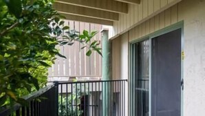 Un balcón con baranda de metal negro, puerta corrediza de vidrio y piso de madera.